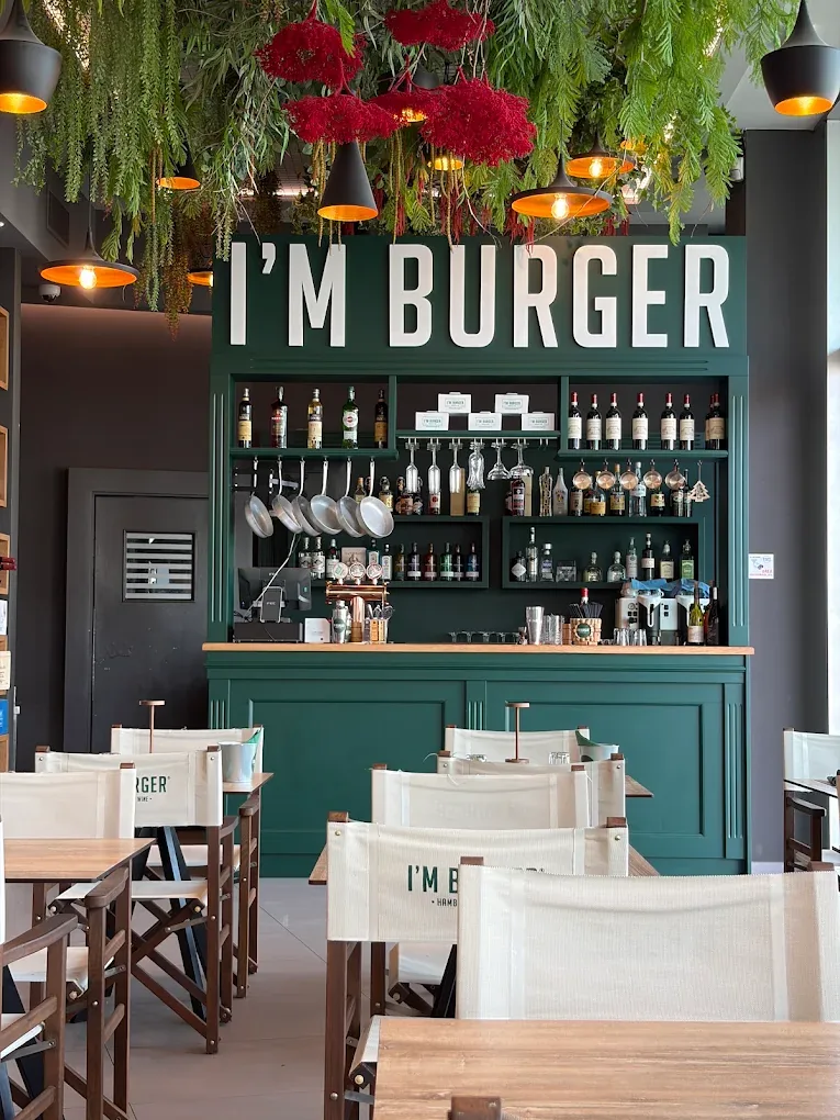 Sala di I'm Burger: bancone verde bottiglia, bottiglie di vino, sedie da regista e piante pensili